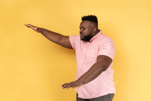 Side view of lonely blind disabled man wearing pink shirt standing with closed eyes and outstretched hands searching way, walking with doubts. Indoor studio shot isolated on yellow background.