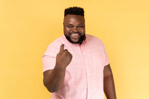 Come to me. Portrait of man wearing pink shirt making beckoning gesture, inviting for date and looking alluring, flirting to camera. Indoor studio shot isolated on yellow background.