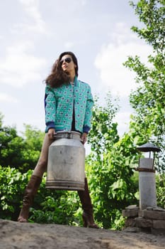 Young fashionable farmer woman posing on camera while holding milk can.