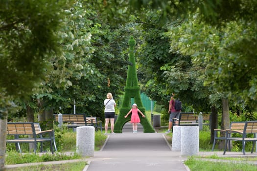 Moscow, Russia - July 9. 2023. Family with a child near a garden sculpture in the form of an Eiffel Tower on the boulevard in Zelenograd