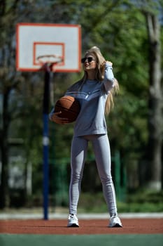 athletic blonde girl stands on the basketball court in a gray tracksuit with a ball in her hands