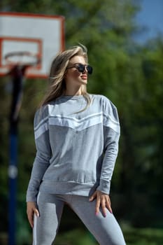 athletic blonde girl stands on the basketball court in a gray tracksuit
