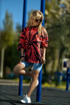 blonde athletic girl stands on the sports ground in a t-shirt, breeches, white sneakers and white headphones