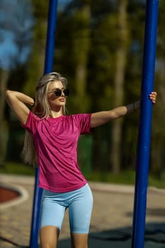 blonde athletic girl stands on the sports ground in a t-shirt, breeches, white sneakers and white headphones