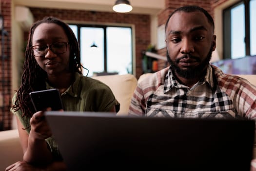 Couple having communication problems not talking to each other and using digital devices ignoring each other. Woman browsing social media on smartphone while man is working on laptop.