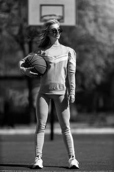 athletic blonde girl stands on the basketball court in a gray tracksuit with a ball in her hands black and white