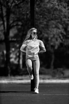 blonde athletic girl stands on the basketball court in a gray sportswear leaning on a basketball hoop black and white