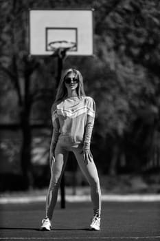 athletic blonde girl stands on the basketball court in a gray tracksuit black and white