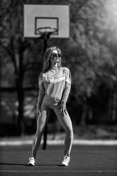 athletic blonde girl stands on the basketball court in a gray tracksuit black and white
