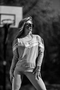 athletic blonde girl stands on the basketball court in a gray tracksuit black and white