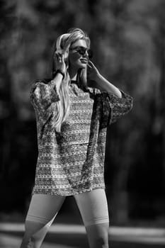 blonde athletic girl stands on the football field in a T-shirt, breeches, white sneakers and white headphones black and white