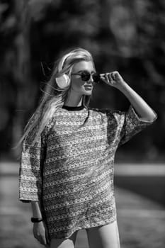 blonde athletic girl stands on the football field in a T-shirt, breeches, white sneakers and white headphones black and white