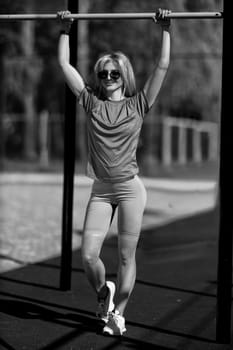 blonde athletic girl stands on the sports ground in a t-shirt, breeches, white sneakers and white headphones black and white