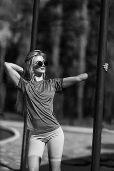 blonde athletic girl stands on the sports ground in a t-shirt, breeches, white sneakers and white headphones black and white