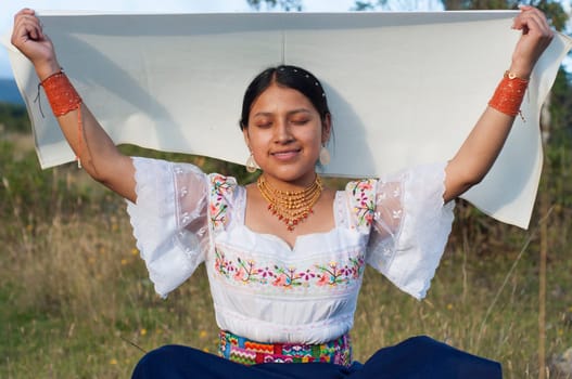 indigenous woman sitting in the amazon of ecuador in traditional dress of her culture and holding a white veil aloft in a ritual. High quality photo