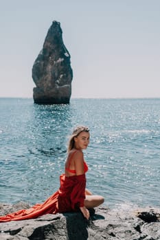 Woman travel sea. Young Happy woman in a long red dress posing on a beach near the sea on background of volcanic rocks, like in Iceland, sharing travel adventure journey