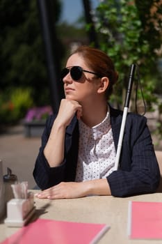 A blind woman in a business suit is sitting in an outdoor cafe