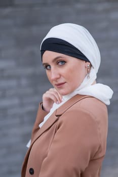 Portrait of a young blue-eyed woman in a hijab against a gray brick wall. A Muslim woman looks at the camera turning around