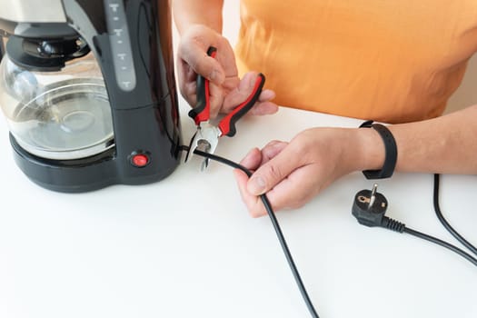 A man is sitting at a table, repairing a small coffee maker with a screwdriver. Close-up