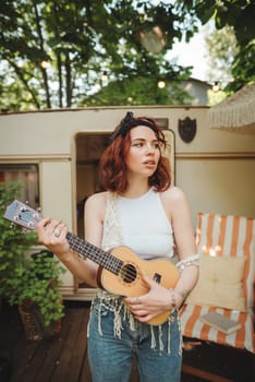 Happy hippie girl is having a good time with playing on guitar in camper trailer. Holiday, vacation, trip concept.High quality photo