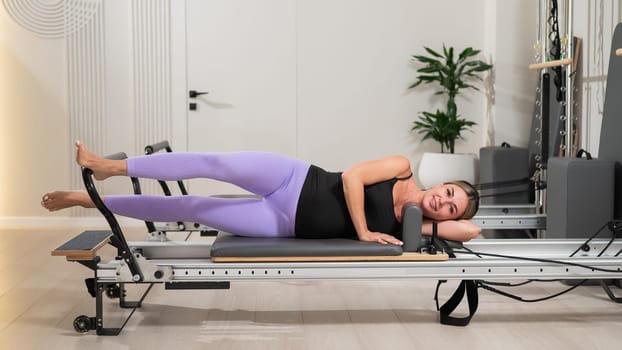 A young pregnant woman is practicing Pilates on a reformer. Exercises for the expectant mother.