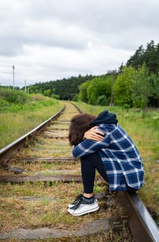 Stress, sadness, loneliness, pain. An upset girl sits on the rails, a psychological situation, help and support. Vertical photo