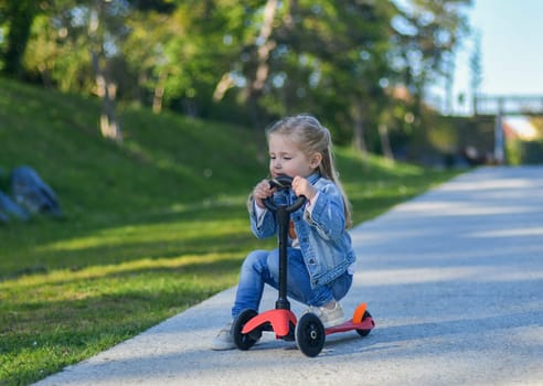 Little girl of 3 years old is riding a scooter