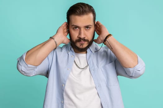 Dont want to hear and listen. Frustrated annoyed irritated lebanese man covering ears gesturing No, avoiding advice ignoring unpleasant noise loud voices. Handsome arabian guy alone on blue background