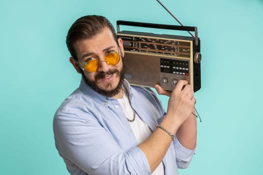 Young lebanese man using retro tape record player to listen music, disco dancing of favorite track, having fun, entertaining, fan of vintage technologies. Arabian guy isolated on blue background
