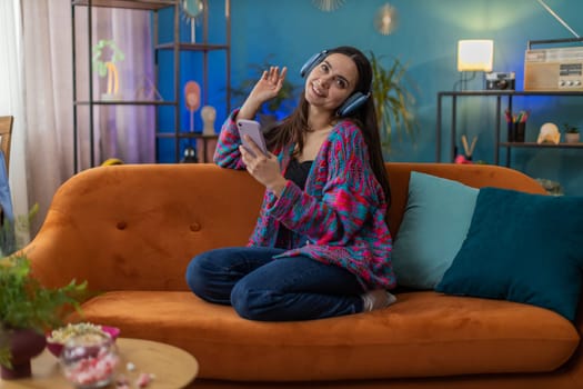 Happy overjoyed Caucasian woman in wireless headphones relaxing sitting on couch at home apartment choosing listening favorite energetic disco dancing music. People weekend daytime leisure activities