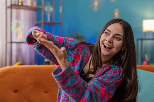 Cheerful rich young woman showing wasting or throwing money around hand gesture, more tips earnings, big profit, win lottery, body language, share. Portrait of girl at home apartment room on sofa