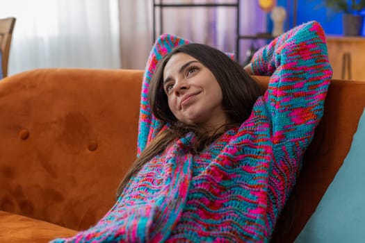 Tired Caucasian woman lying down on comfortable couch taking a rest daytime nap. Portrait of carefree young girl holding hands behind head relaxing falling asleep at home apartment living room on sofa