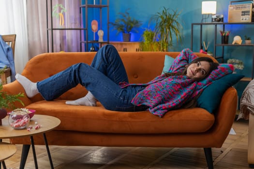 Tired pretty woman lying down on comfortable couch, taking a rest, daytime nap. Portrait of carefree young girl holding hands behind head relaxing, falling asleep at home apartment living room on sofa