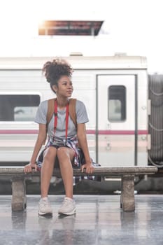 Young Asian African woman traveler with backpack in the railway train station, traveler girl walking stand sit waiting take a picture on railway platform train station. High quality photo..