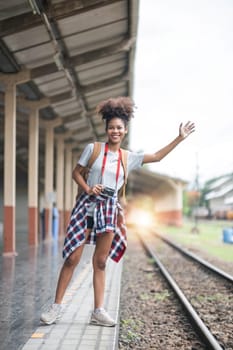 Young Asian African woman traveler with backpack in the railway train station, traveler girl walking stand sit waiting take a picture on railway platform train station. High quality photo..