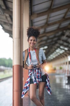 Young Asian African woman traveler with backpack in the railway train station, traveler girl walking stand sit waiting take a picture on railway platform train station. High quality photo..