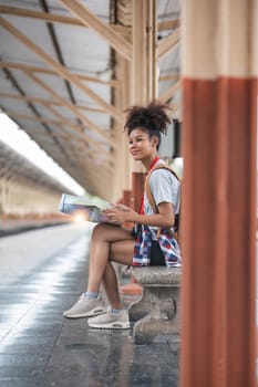 Young woman female smiling traveler with back pack looking to map while waiting for the train at train station. High quality photo..