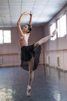 Graceful Asian ballerina in a beige bodysuit and black skirt is rehearsing in a dance class