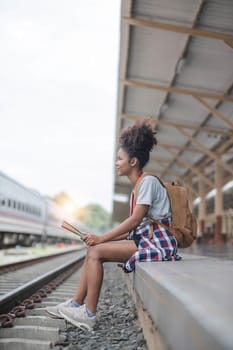 Young woman female smiling traveler with back pack looking to map while waiting for the train at train station. High quality photo..