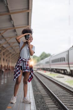 Young Asian African woman traveler with backpack in the railway train station, traveler girl walking stand sit waiting take a picture on railway platform train station. High quality photo..