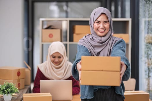 A happy young Asian Muslim female online seller working with her employee in the office. SME business, online shop owner..