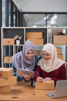 Friend muslim female work independent business sme online shopping working on laptop computer with parcel box on desk at home, SME online business and delivery concept..