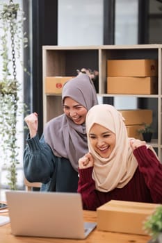 Two women muslim look at online product sales data on laptops and show joy..