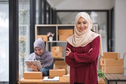 A happy young Asian Muslim female online seller working with her employee in the office. SME business, online shop owner..