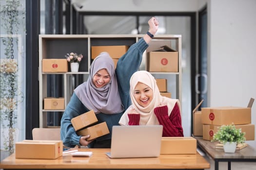 Two women muslim look at online product sales data on laptops and show joy..