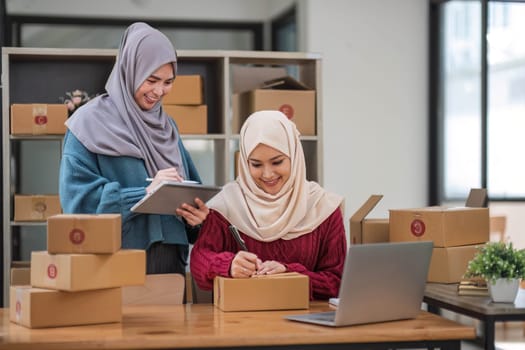 Friend muslim female work independent business sme online shopping working on laptop computer with parcel box on desk at home, SME online business and delivery concept..