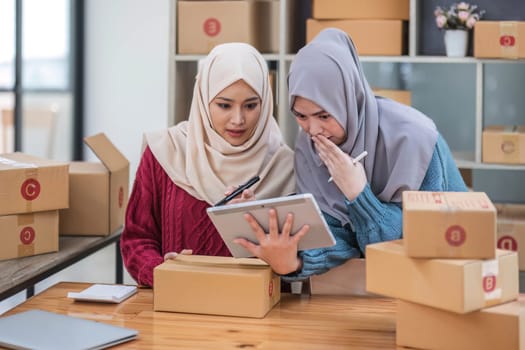 Friend muslim female work independent business sme online shopping working on laptop computer with parcel box on desk at home, SME online business and delivery concept..