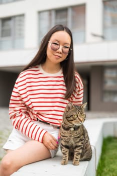 Young woman and tabby cat sitting on a bench outdoors