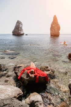 Woman travel sea. Young Happy woman in a long red dress posing on a beach near the sea on background of volcanic rocks, like in Iceland, sharing travel adventure journey