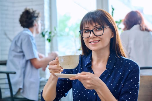 Relaxed happy middle aged woman enjoying fragrant fresh tasty cup of coffee while sitting in coffee shop. Coffee culture, lifestyle, people concept